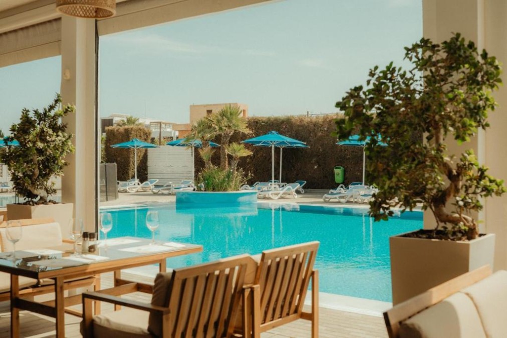 Terrasse repas au bord de la piscine avec tables, plantes et vue sur la piscine extérieure.
