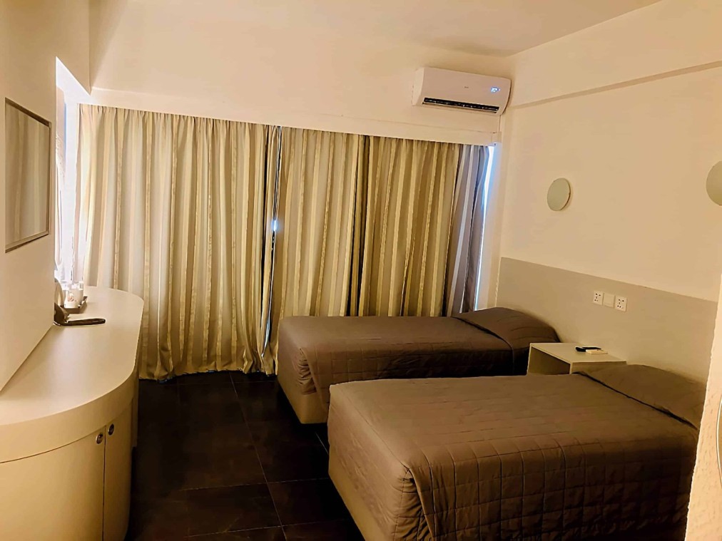 Chambre twin avec deux lits simples, climatisation et rideaux sur toute la largeur.