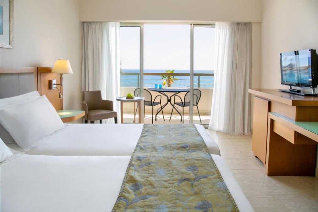 Chambre d'hôtes avec balcon vue mer, lits jumeaux, télévision et coin bureau.