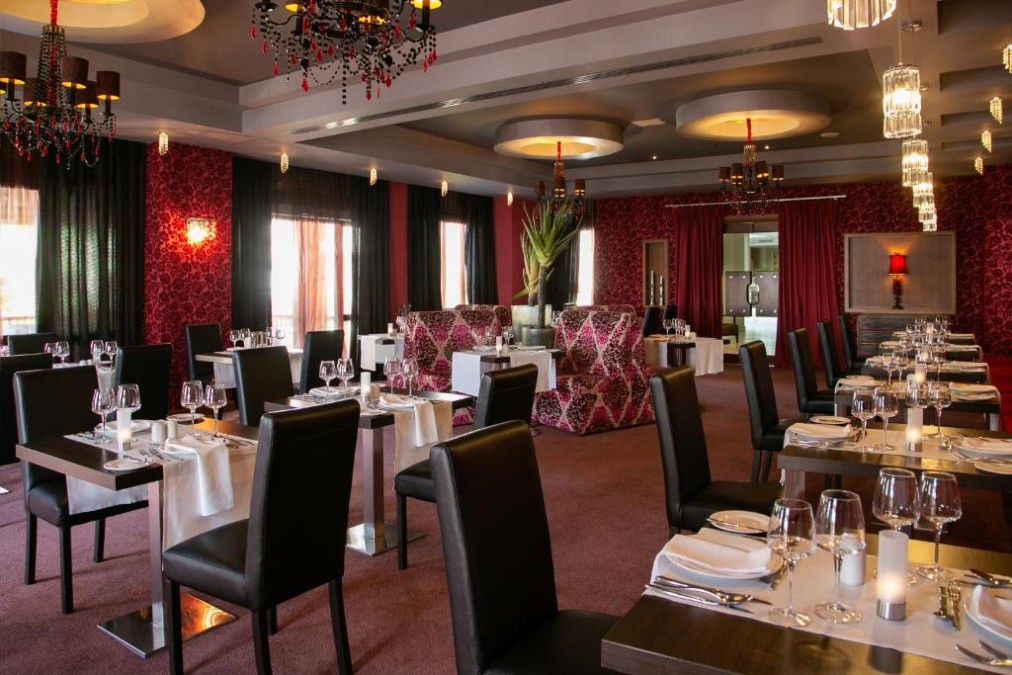 Salle de restaurant avec tables dressées, lustres et sièges à motifs.