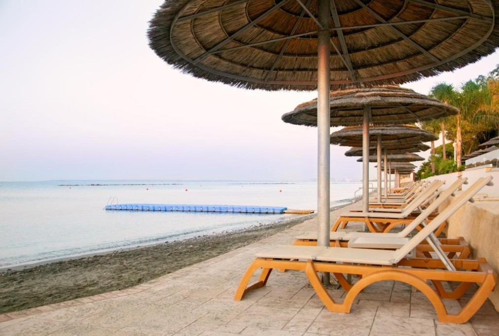 Chaises longues en bord de mer sous des parasols au bord d'une mer calme avec ponton flottant.