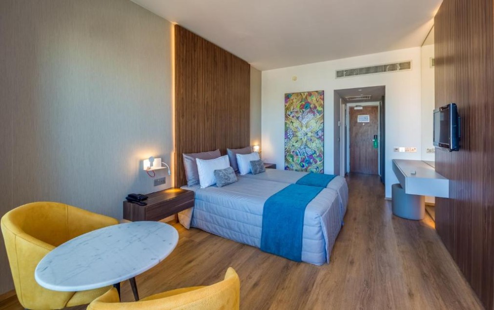 Chambre avec lit double, coin salon et télévision murale.